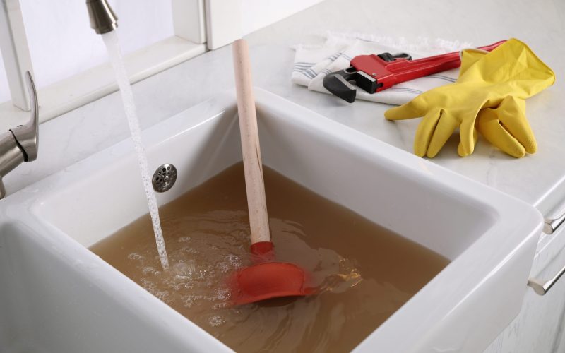 Kitchen counter with clogged sink, plunger and plumber's accessories
