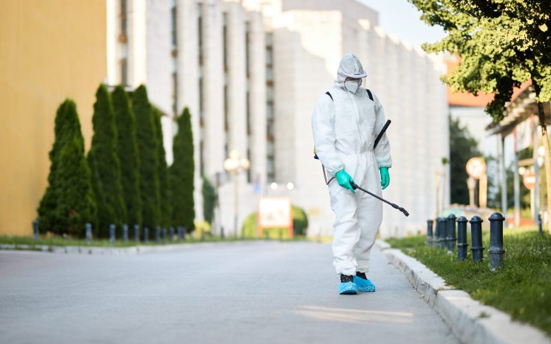 Disinfectant worker in protective suit sanitizing empty city streets during COVID-19 epidemic.