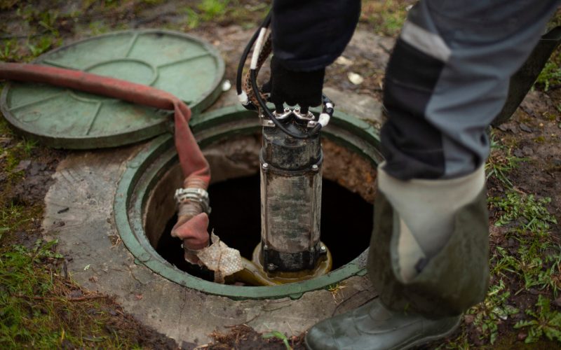 Sewer repair. The worker lowers the equipment into the sewer hatch. Installation of the hydrant in the underground water supply system.