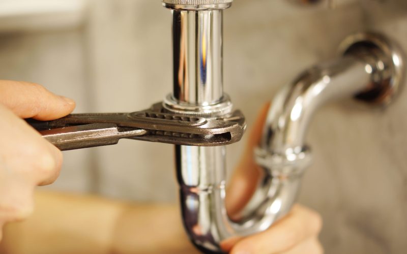 Plumbing repair service. Professional installer with spanner checking pipe.